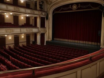 Leerer Theatersaal mit roten Sitzreihen und geschlossenem Bühnenvorhang, gesehen vom ersten Rang